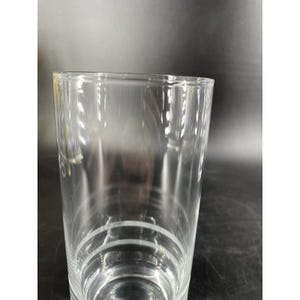 May include: A clear, cylindrical glass with a slightly flared rim. The glass has three horizontal etched lines near the base. The glass is transparent, suitable for beverages. The height is approximately 15 cm.