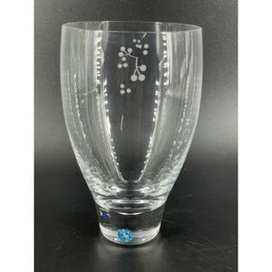 May include: A clear glass vase with a flared top and a rounded base. The vase features etched floral designs and vertical lines. A blue and white sticker is visible at the base. The vase is likely used for decorative purposes.