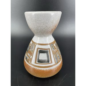 May include: A ceramic vase with a unique hourglass shape. The top and bottom sections are a warm, earthy brown, while the middle section features a geometric pattern in black, brown, and white. The vase has a textured, speckled finish.