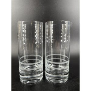 May include: A pair of clear, highball glasses. Each glass has a simple design with two etched horizontal bands near the base. These glasses are ideal for serving water, juice, or cocktails. The glasses are approximately 15 cm tall.