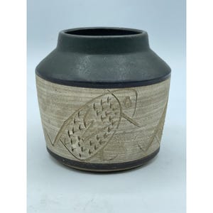 以下が含まれることがあります： 手作りのセラミック花瓶。濃い緑色のトップとベージュのボディ。ボディにはエッチングされた魚のデザインがあります。花瓶は丸い形で、濃い茶色のベースです。