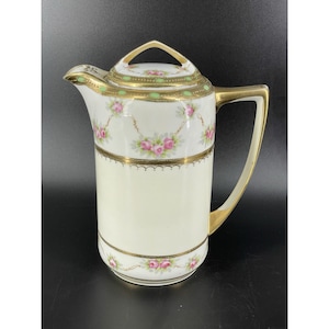May include: Cream-colored porcelain pitcher with a gold handle and trim. The pitcher features pink rose garlands and green accents. The lid has a gold handle and is also decorated with pink roses and green accents. A decorative piece.
