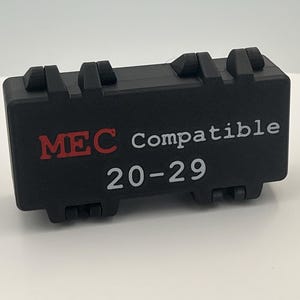 May include: A rectangular black plastic storage case with two hinged latches on the top and bottom edges. The front surface features the red text MEC, the white text Compatible, and the white numerical text 20-29 printed in a clear sans-serif font.