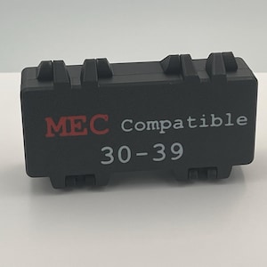 May include: A rectangular black plastic storage case with two hinged latches on the top and bottom. The front of the case features the red text MEC, the white text Compatible, and the white numerical text 30-39 printed on the center surface.