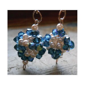 May include: A pair of dangle earrings featuring clusters of faceted blue crystal beads and small white pearls. Each earring is suspended from a circular metal hoop, showcasing a spherical arrangement of alternating blue crystals and white pearls.