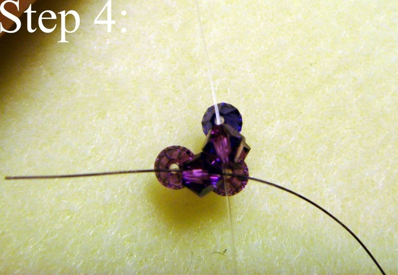 Peut inclure: Gros plan d'une &eacute;tape d'un projet de perlage. L'image montre un groupe de perles violettes, dont des cristaux facett&eacute;s et des perles rondes, enfil&eacute;es sur un fil fonc&eacute;. Le texte "&Eacute;tape 4 :" est dans le coin sup&eacute;rieur gauche.