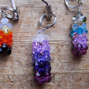 May include: Three beaded charms. The charm on the left has a rainbow colour scheme, the middle charm is purple, and the charm on the right has a blue and purple colour scheme. Each charm has a silver metal ring.