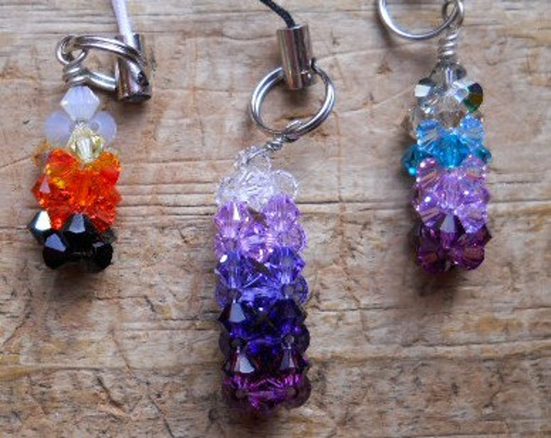 Peut inclure: Trois breloques perl&eacute;es align&eacute;es. La breloque de gauche est multicolore, celle du milieu est violette et celle de droite est bleue et violette. Chaque breloque a un anneau en m&eacute;tal argent&eacute;.