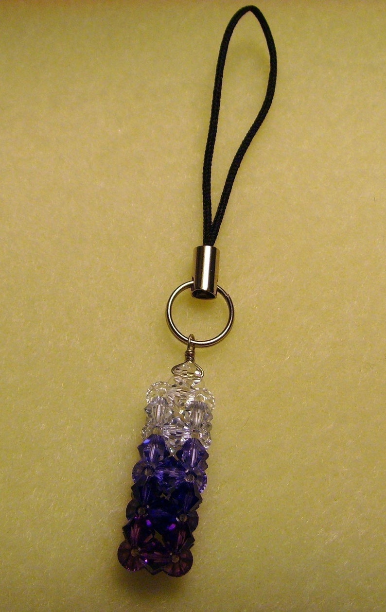 Peut inclure: Un porte-cl&eacute;s ou breloque de t&eacute;l&eacute;phone orn&eacute; de perles d&eacute;grad&eacute;es transparentes, violettes et violet fonc&eacute;. Il comporte une boucle en cordon noir, un anneau argent&eacute; et un tube en m&eacute;tal argent&eacute;.