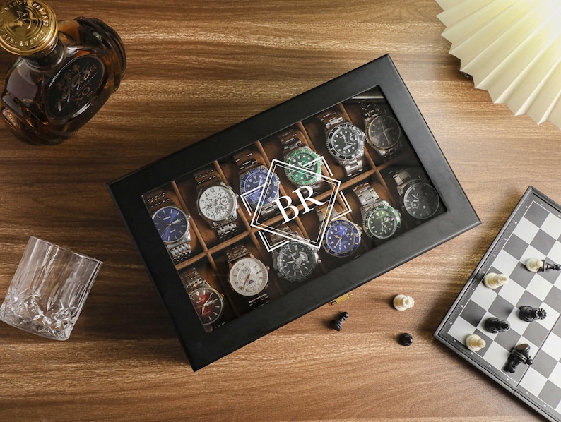 May include: A black watch display case with a glass top, filled with various wristwatches. The watches have different colored faces and bands. The initials "BR" are superimposed on the watches. A chess board and a glass are also visible.