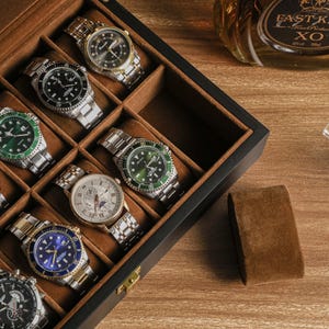 May include: A collection of wristwatches in a wooden display case. The watches feature various face colors, including black, blue, and green, with silver and gold bands. A bottle of Fast King XO cognac and a glass are visible in the background.