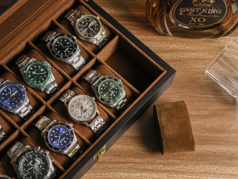 May include: A collection of wristwatches in a wooden display case. The watches feature various face colors, including black, blue, and green, with silver and gold bands. A bottle of Fast King XO cognac and a glass are visible in the background.