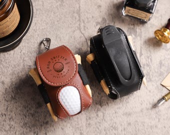 May include: Two leather golf ball holders, one brown and one black, each with a clip and tee holders. The brown holder has a golf ball and the text "RON SWITZER BEST GOLFER".