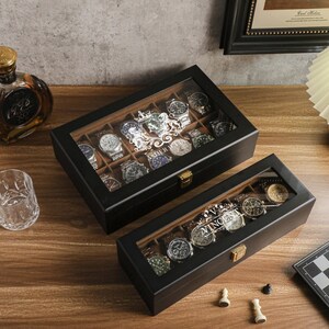 May include: Two black wooden watch display cases with glass tops, filled with various wristwatches. A bottle of liquor, a drinking glass, and a chessboard are also on the wooden surface.