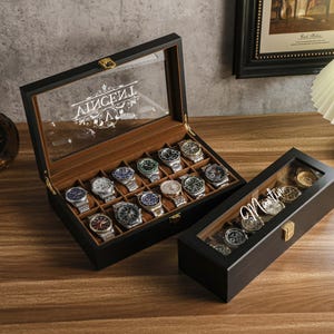 May include: Two black wooden watch display cases with glass lids. One case is open, revealing multiple watches. The other case is closed, with the name "Martin" in script on the lid. A bottle of liquor and a glass are in the background.