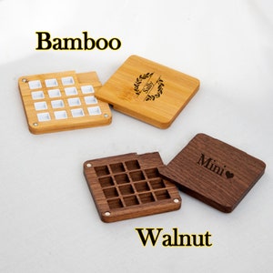 Op de afbeelding: Twee houten dozen met deksels, een van bamboe en de andere van walnoot. De bamboe doos heeft een wit deksel met een kransontwerp en de naam "Sally" erop gegraveerd. De walnootdoos heeft een deksel met het woord "Mini" en een hartje erop gegraveerd.