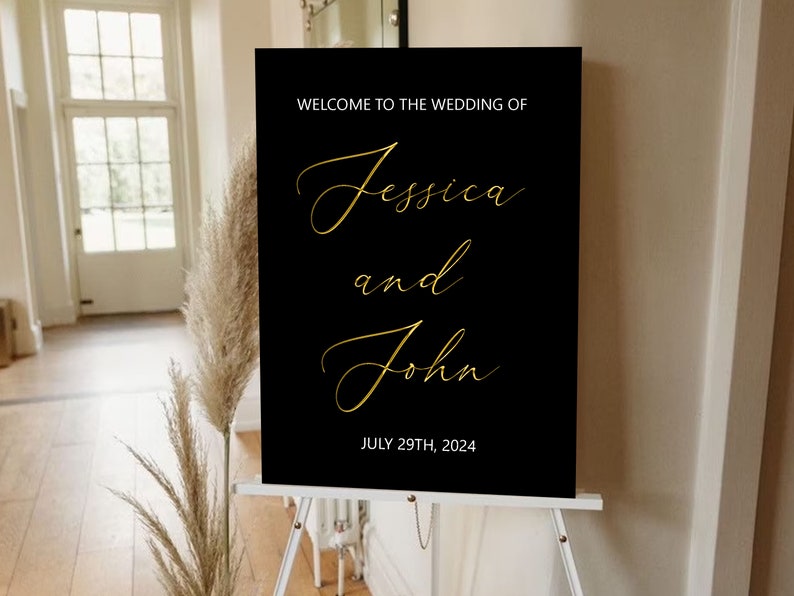 Puede incluir: Un cartel de bienvenida de boda negro con letras doradas. El cartel dice "Bienvenido a la boda de Jessica y John, 29 de julio de 2024".