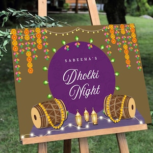 May include: A purple and gold sign with the text "Sabeeha's Dholki Night" in a decorative font. The sign is decorated with strings of lights, flowers, and two drums.