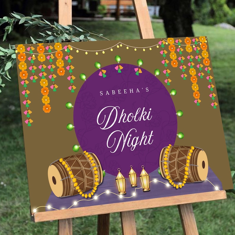 May include: A purple and gold sign with the text "Sabeeha's Dholki Night" in a decorative font. The sign is decorated with strings of lights, flowers, and two drums.