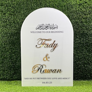Puede incluir: Un cartel blanco en forma de arco con letras doradas. El cartel dice "بسم الله الرحمن الرحيم"  "WELCOME TO OUR BEGINNING" "Fady & Rawan" "AND HE PUT BETWEEN YOU LOVE AND MERCY" "04.03.25".