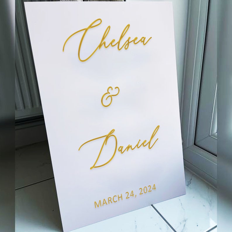 Puede incluir: Un cartel de boda blanco con letras doradas. El cartel dice "Chelsea & Daniel" y "March 24, 2024".