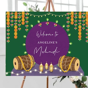 May include: A purple and green welcome sign with the text "Welcome to Angeline's Mehndi" decorated with yellow and pink floral garlands, string lights, and two drums with gold beads.