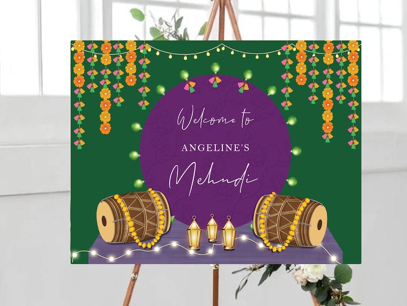 May include: A purple and green welcome sign with the text "Welcome to Angeline's Mehndi" decorated with yellow and pink floral garlands, string lights, and two drums with gold beads.