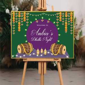 May include: Welcome to Ambia's Dholki Night sign with a purple circle background, two brown drums with yellow beads, and gold lanterns on a green background with yellow and pink floral garlands.