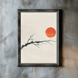 May include: A framed print of a minimalist black branch with a large orange sun in the background. The print has a white background and is framed in a dark gray frame.
