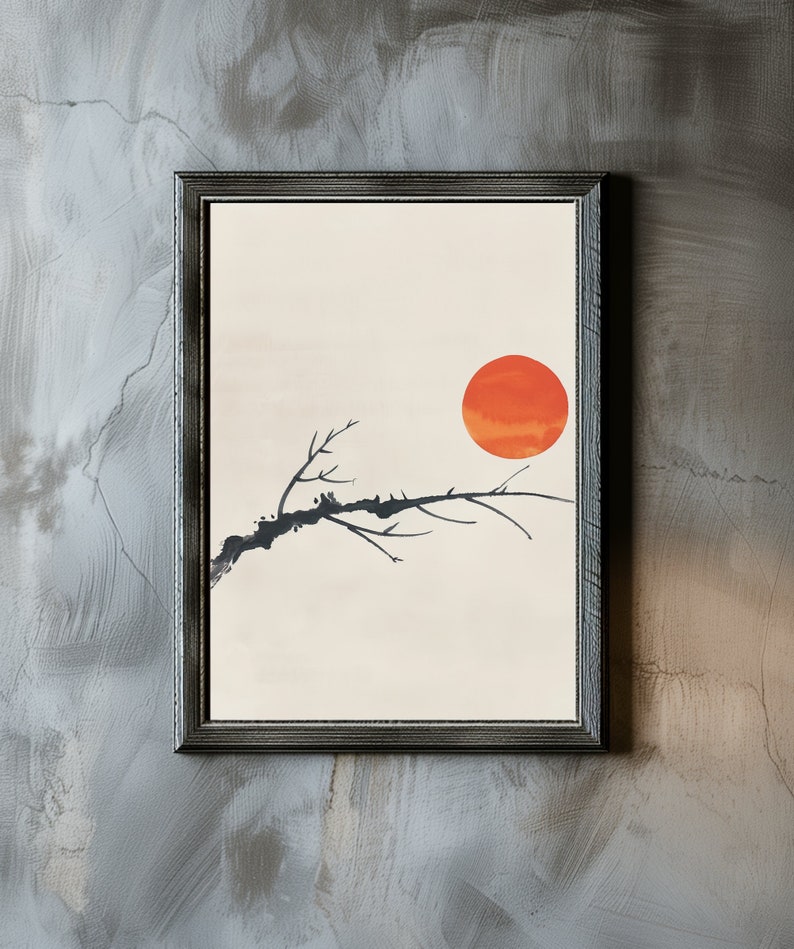 May include: A framed print of a minimalist black branch with a large orange sun in the background. The print has a white background and is framed in a dark gray frame.
