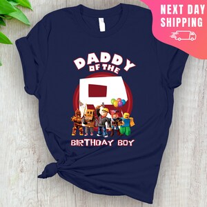 May include: Navy blue t-shirt with the text "Daddy of the" and a red circle with a white letter "R" inside.  There are five cartoon figures standing in front of the circle, including a figure with a red balloon. The text "Birthday Boy" is below the circle.