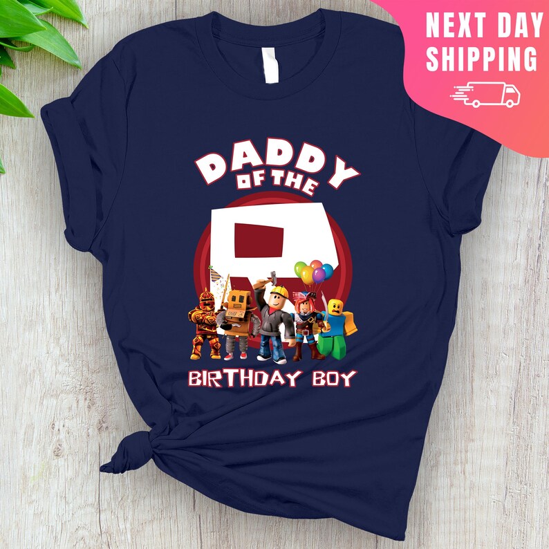 May include: Navy blue t-shirt with the text "Daddy of the" and a red circle with a white letter "R" inside.  There are five cartoon figures standing in front of the circle, including a figure with a red balloon. The text "Birthday Boy" is below the circle.