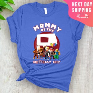 May include: Blue t-shirt with the text "Mommy of the Birthday Boy" and a red Roblox logo with Roblox characters.