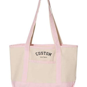May include: A pink and beige canvas tote bag with a front pocket and the text "CUSTOM text here" in black.