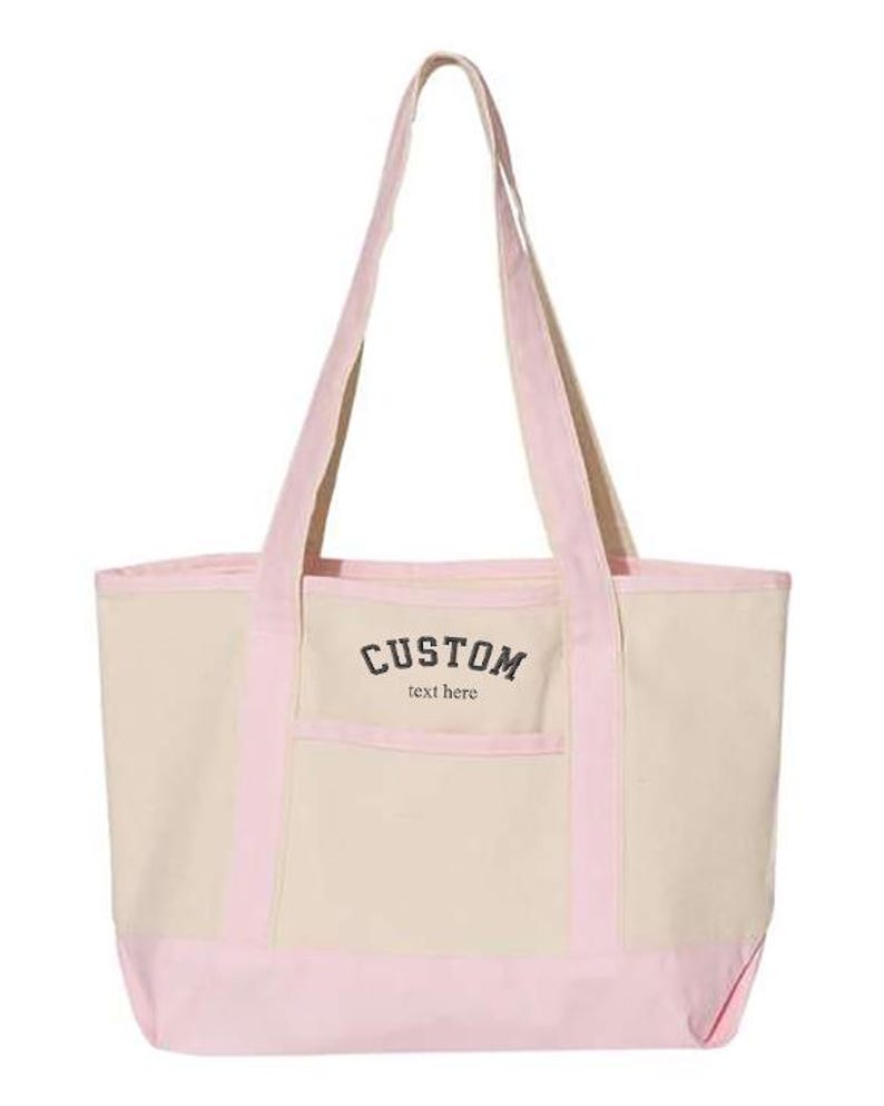 May include: A pink and beige canvas tote bag with a front pocket and the text "CUSTOM text here" in black.
