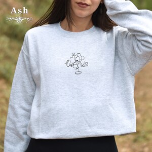 May include: A gray sweatshirt with a black line drawing of Mickey Mouse on the front. The drawing shows Mickey Mouse with his arms raised and a circle around his head.