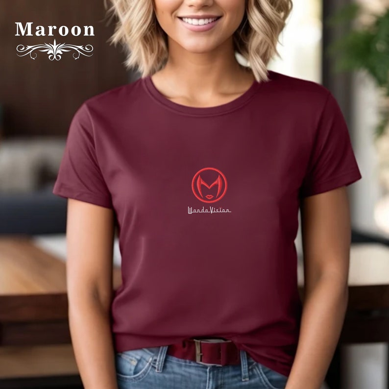 May include: A maroon t-shirt with a red WandaVision logo featuring a stylised Wanda Maximoff face inside a circle. The text "WandaVision" is written below the logo.