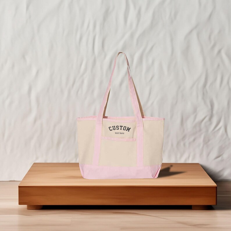 May include: A pink and beige canvas tote bag with a front pocket and the text "CUSTOM text here" printed on the front.