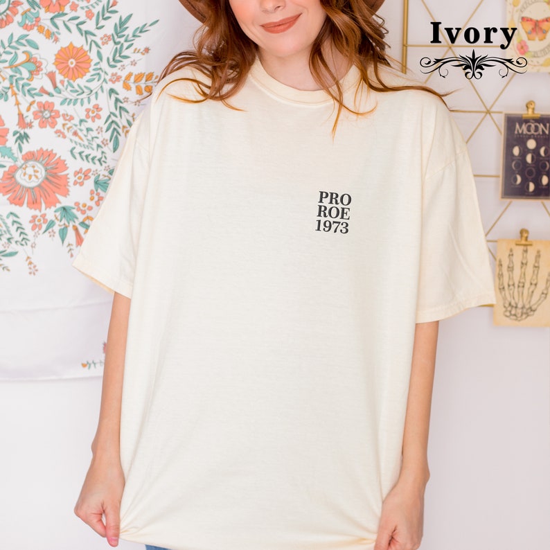 May include: Ivory-colored t-shirt with the text "PRO ROE 1973" printed in black. The shirt has a classic crew neck and short sleeves. The shirt is made of a soft, comfortable material.