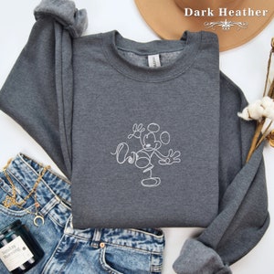 May include: Dark heather grey sweatshirt with a white outline drawing of Mickey Mouse. The sweatshirt is laid out on a denim background.