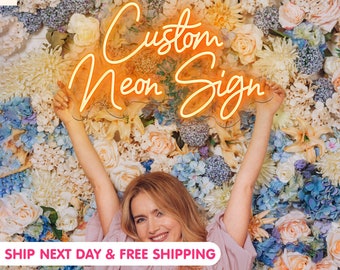 May include: A woman holds up a custom neon sign that says "Custom Neon Sign" in front of a wall of flowers. The sign is orange and yellow and has a wavy border. The woman is smiling and has blonde hair. The flowers are a variety of colors, including pink, white, blue, and yellow.