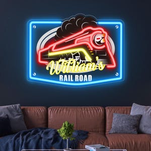 May include: A neon sign depicting a red and yellow train outline with the words "William's Rail Road". The sign has a blue border and is mounted on a dark blue wall above a brown leather sofa.
