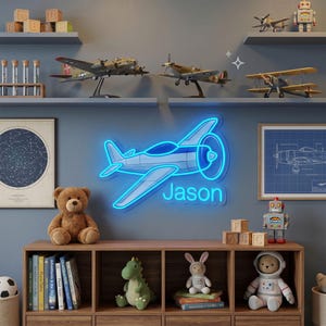 May include: A bright blue neon sign shaped like a propeller airplane with the name Jason illuminated in blue light. The sign is mounted on a dark wall above a wooden bookshelf filled with various toys, books, and model airplanes on shelves.