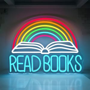 May include: A neon sign with a rainbow arching over an open book. The words "READ BOOKS" are in bright blue neon. The rainbow features red, orange, yellow, green, and blue colors.