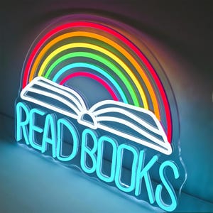 May include: A neon sign featuring a rainbow arching over an open book. The sign is outlined in white and has the words "READ BOOKS" in bright blue neon. The rainbow displays the colors red, orange, yellow, green, and blue.