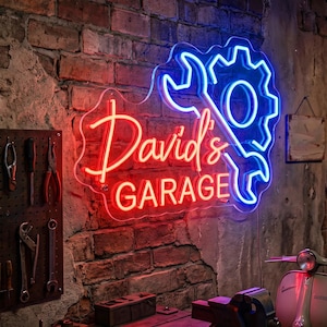 May include: A neon sign for "David's Garage" in red and blue. The sign features a wrench and gear design, with the words "David's" in a cursive font and "GARAGE" in block letters. The sign is mounted on a brick wall.