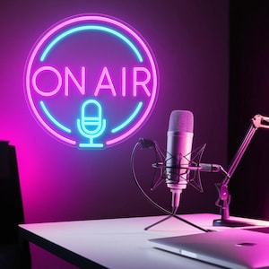 May include: A neon sign with the words "ON AIR" in pink, outlined in blue, above a microphone icon. A silver microphone is positioned on a white desk, with a laptop and microphone stand visible. The background is dark purple.