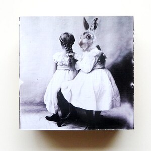 May include: A black and white vintage photograph of two girls in white dresses. One girl is holding a rabbit dressed in a white dress.