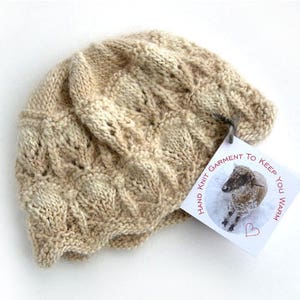 May include: A beige hand-knitted hat with a tag that reads "Hand Knit Garment to Keep You Warm". The tag features a small illustration of a sheep.