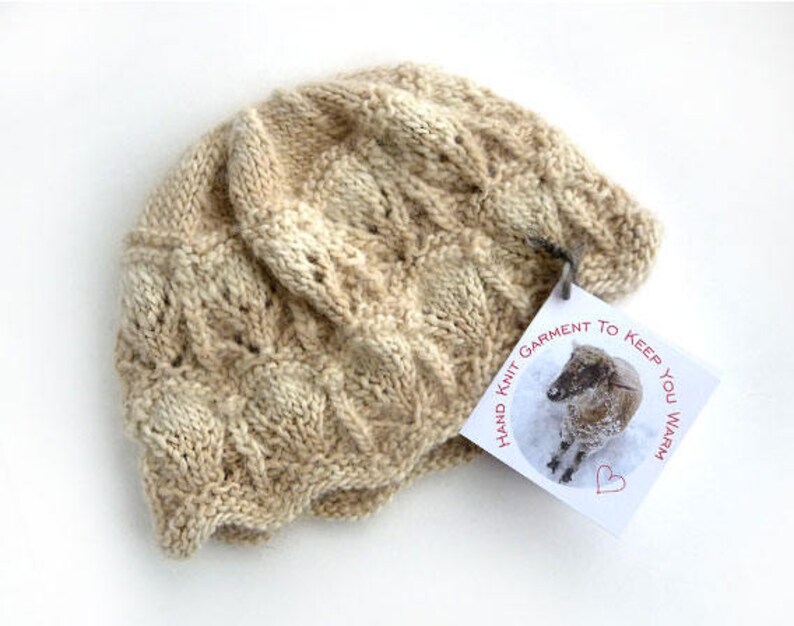 May include: A beige hand-knitted hat with a tag that reads "Hand Knit Garment to Keep You Warm". The tag features a small illustration of a sheep.